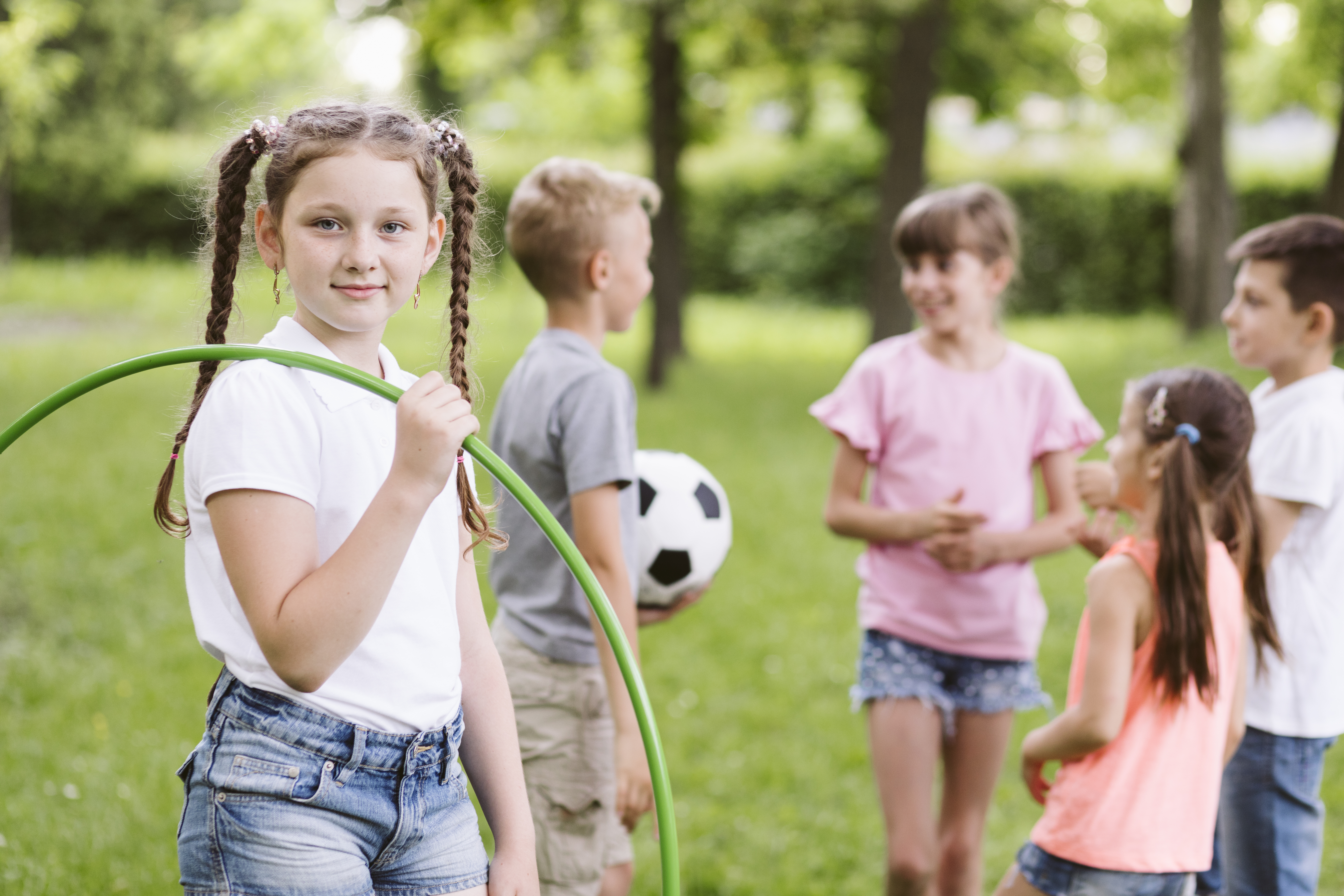 Kinder spielen draußen, eines mit Hula-Hoop, eines mit Ball.
