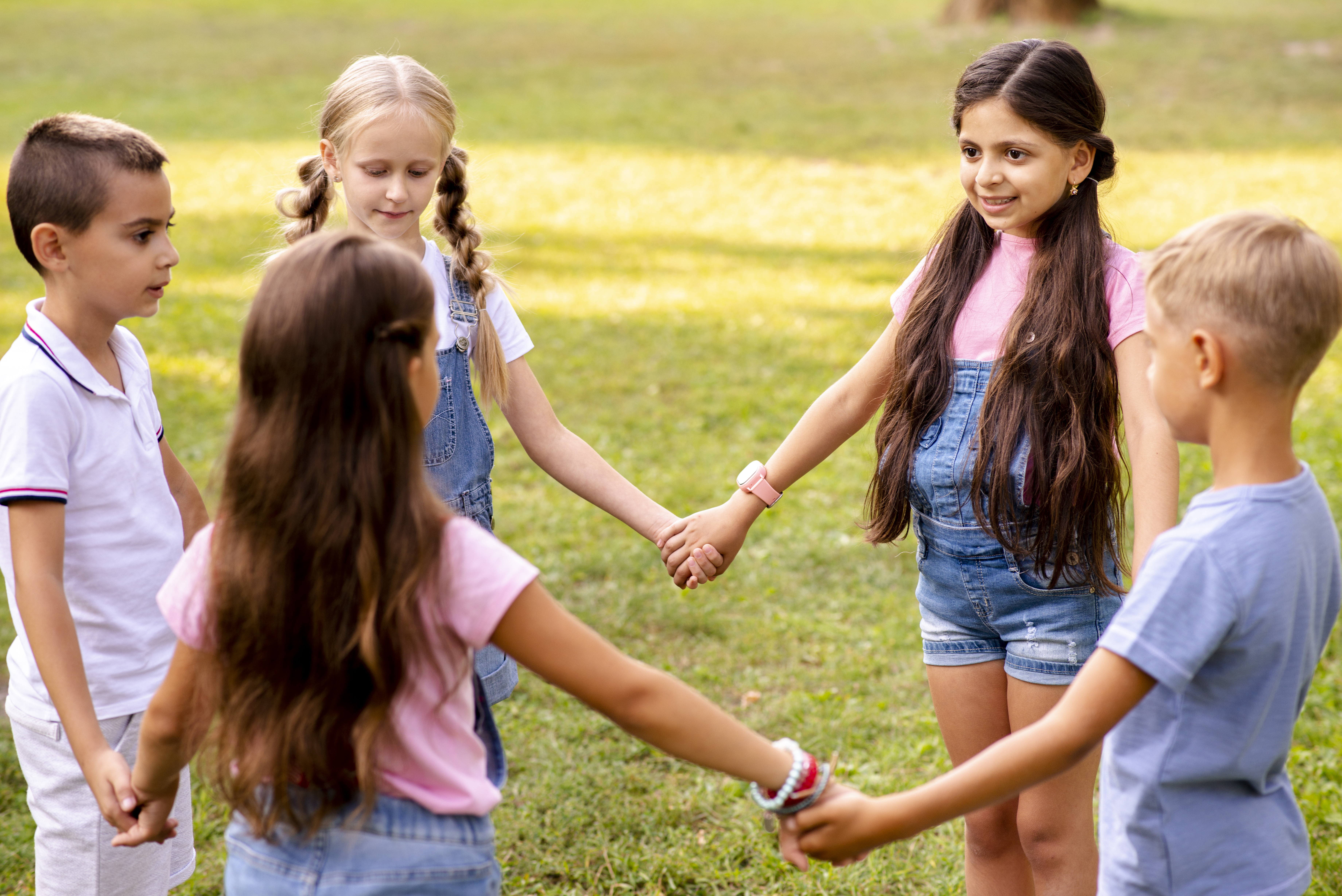 Fünf Kinder im Kreis auf einer Wiese, Gesichter unkenntlich.